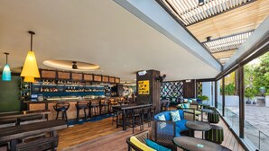 Zona de bar moderna con suelo de madera, taburetes y diferentes opciones de asientos, incluyendo sofás y mesas.