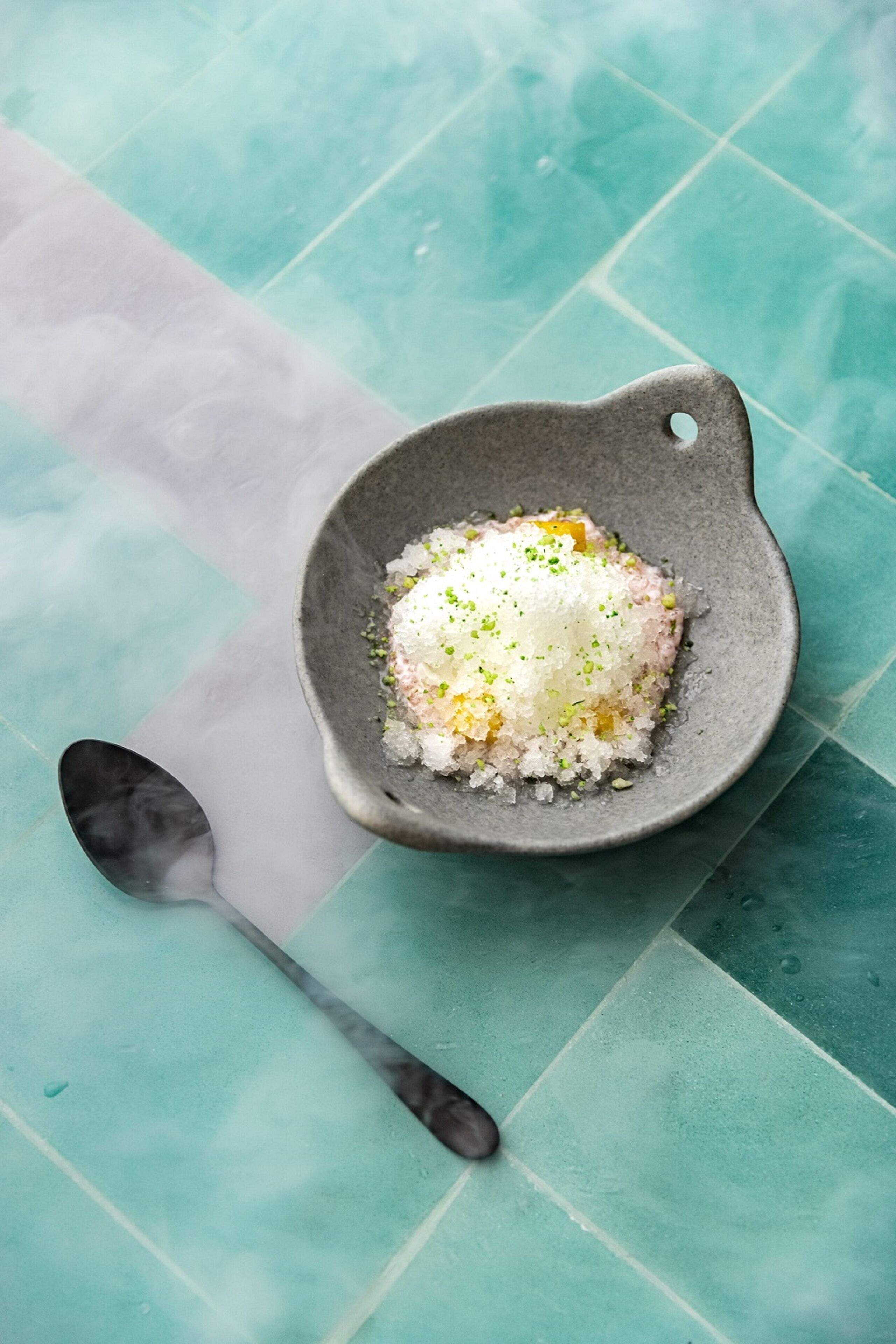 Un tazón de arroz con guarnición verde sobre una superficie de azulejos color turquesa.
