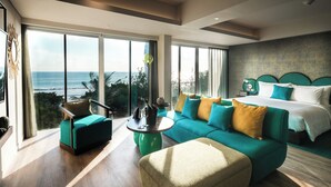 A modern hotel room with a large bed, a teal sofa, and a view of the ocean. - Mamaka Bali (Kuta)