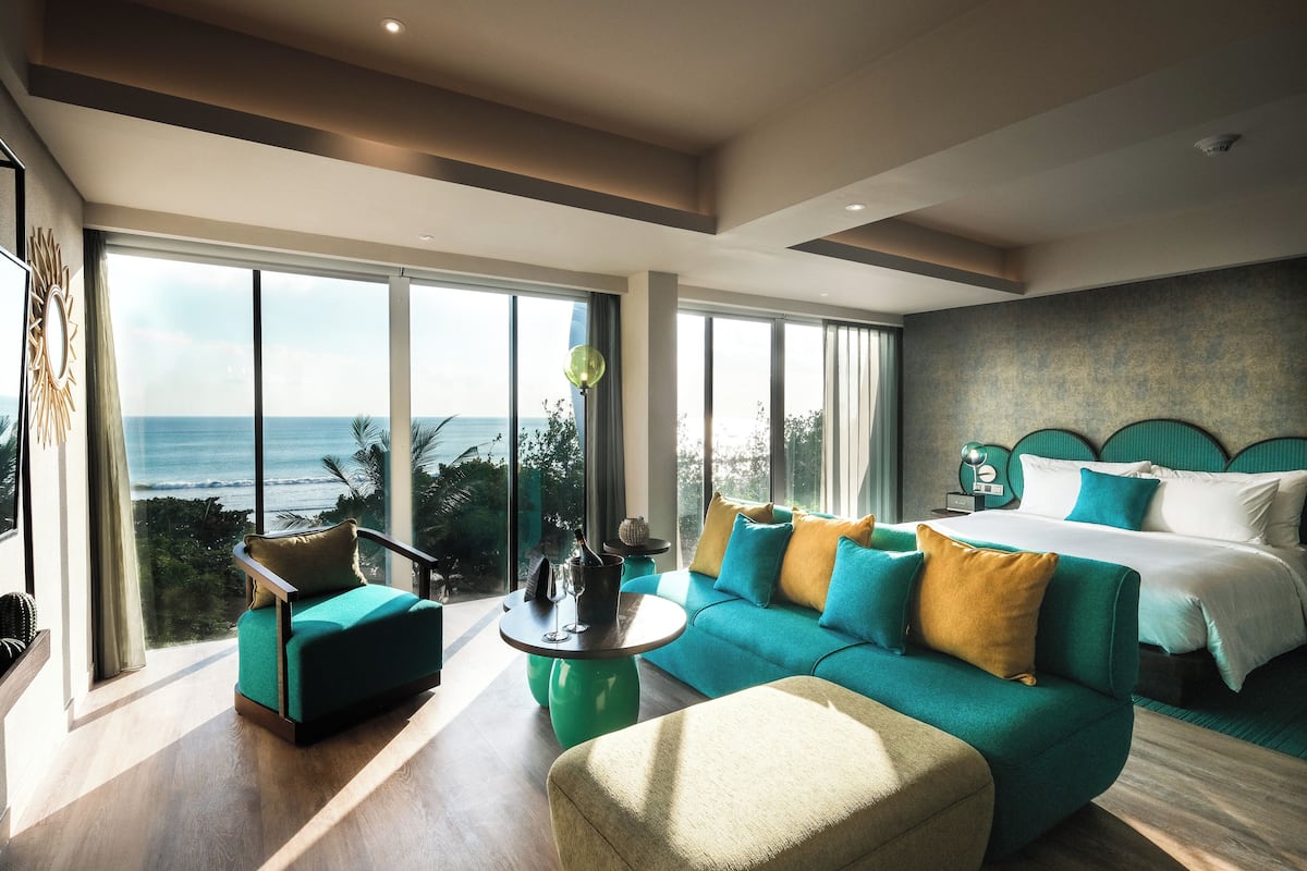 Een moderne hotelkamer met een groot bed, een blauwgroene bank en uitzicht op de oceaan.