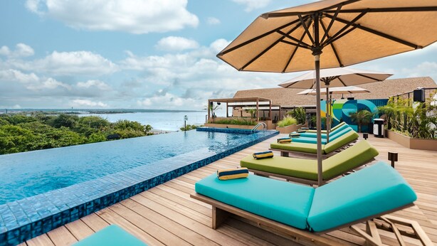 Zona junto a la piscina con sillones de descanso y sombrillas, con vista a una masa de agua.