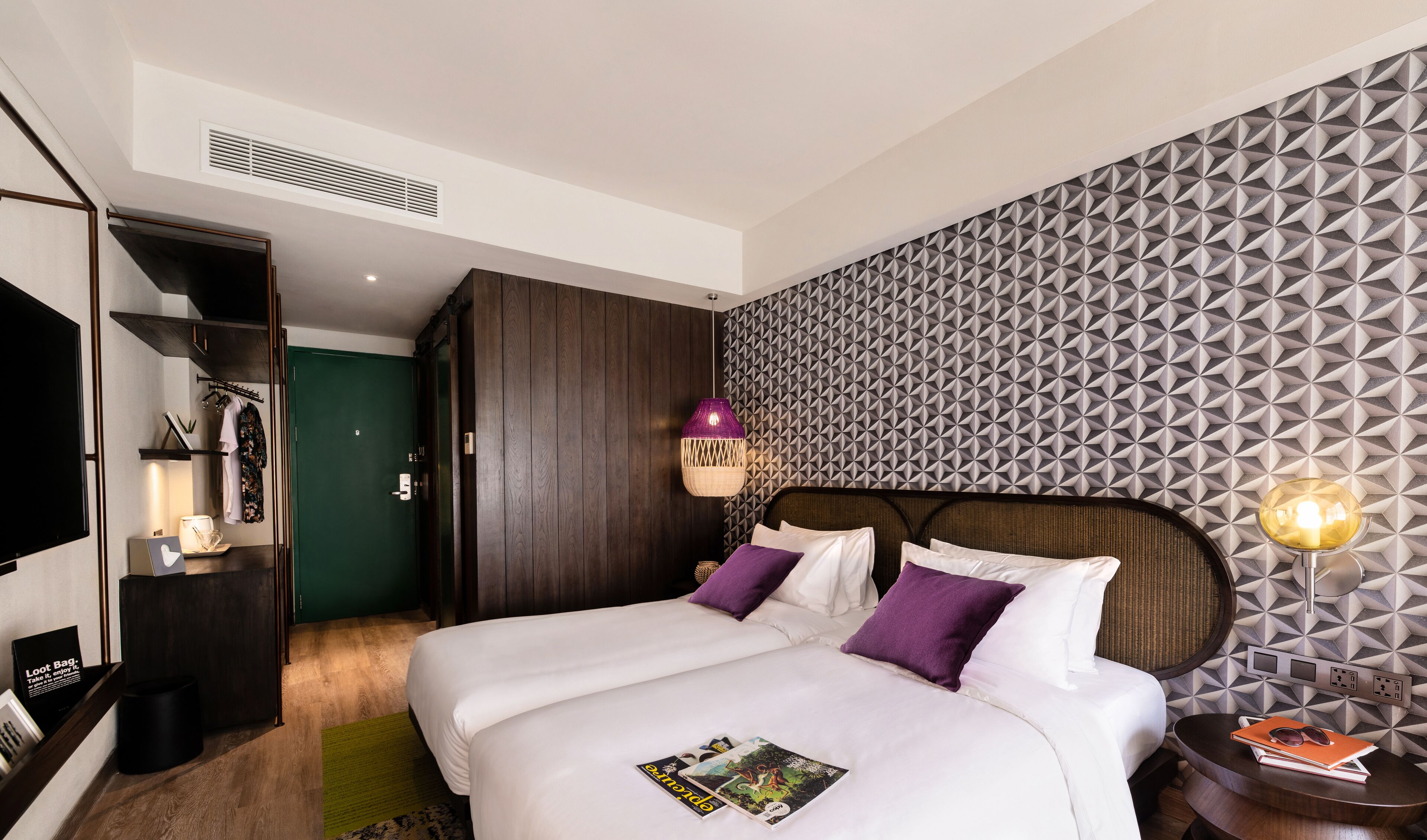Ein modernes Hotelzimmer mit einem großen Bett, einem Kleiderschrank, einem Schminktisch und einer Wand mit geometrischen Mustern.