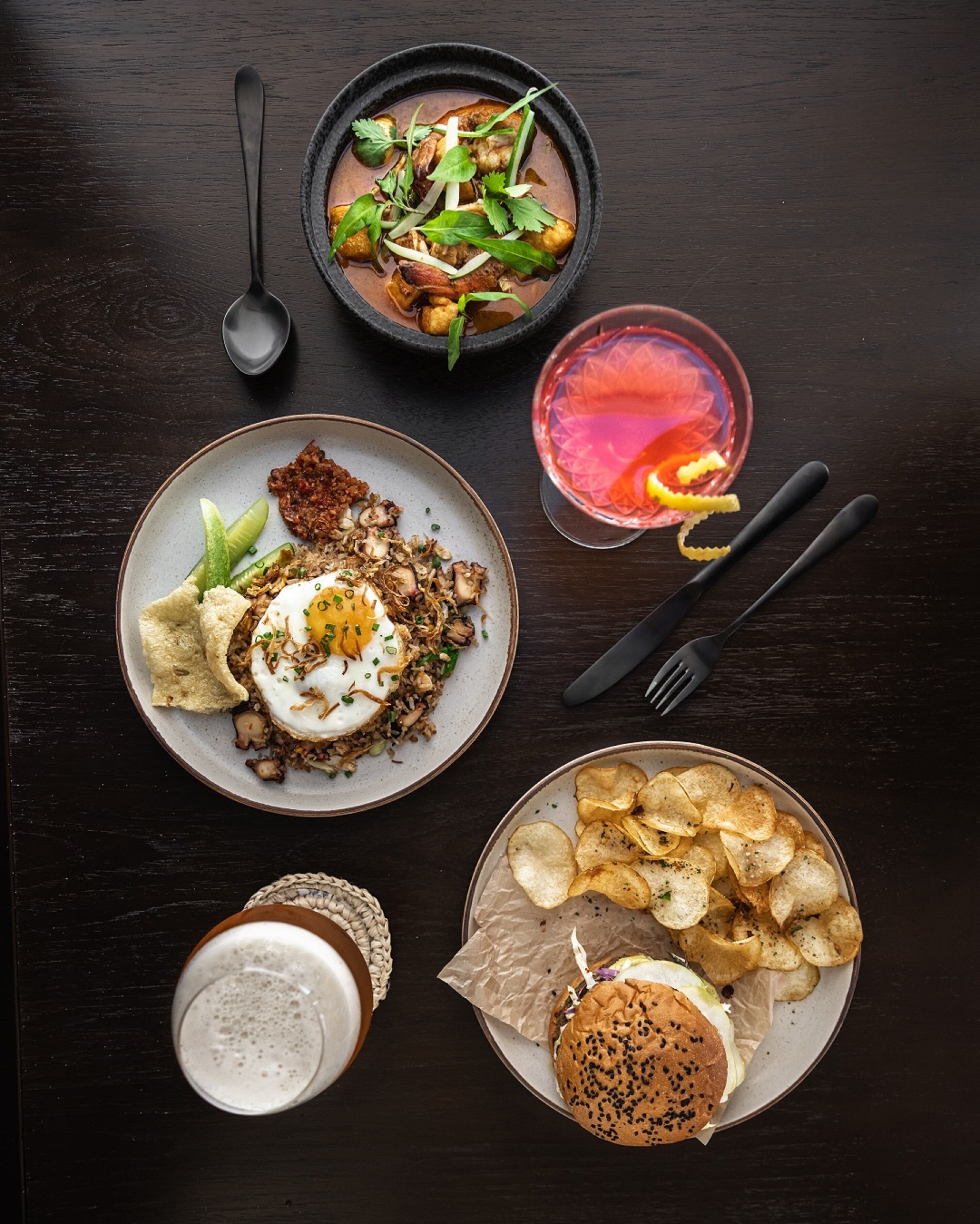 Una mesa con varios platos de comida, incluyendo un tazón de sopa, arroz frito, una hamburguesa, papas fritas y una bebida.