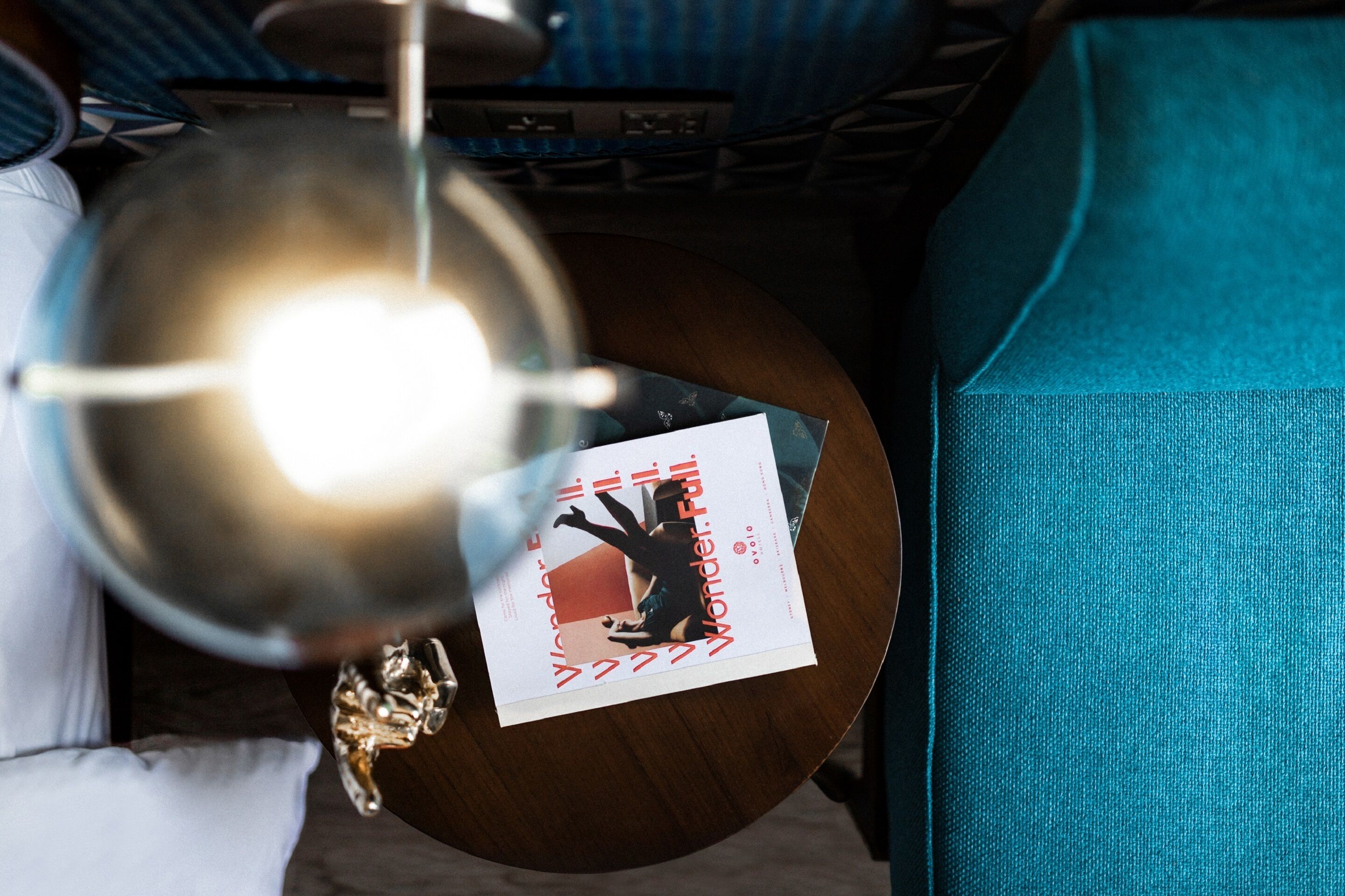 A room with a teal sofa, a wooden side table, and a ceiling light fixture.