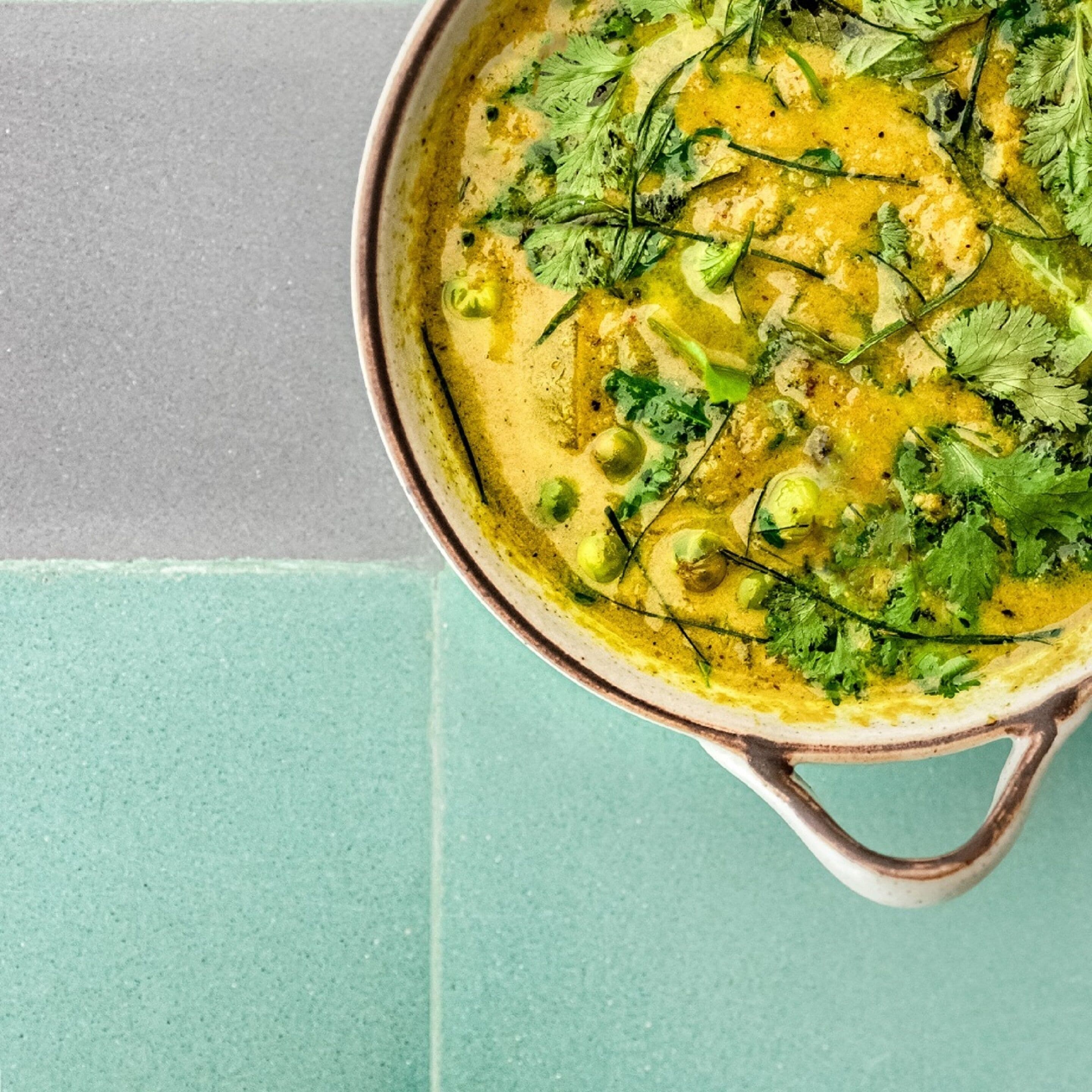 Un plat de curry garni d’herbes vertes, posé sur une surface de couleur turquoise.