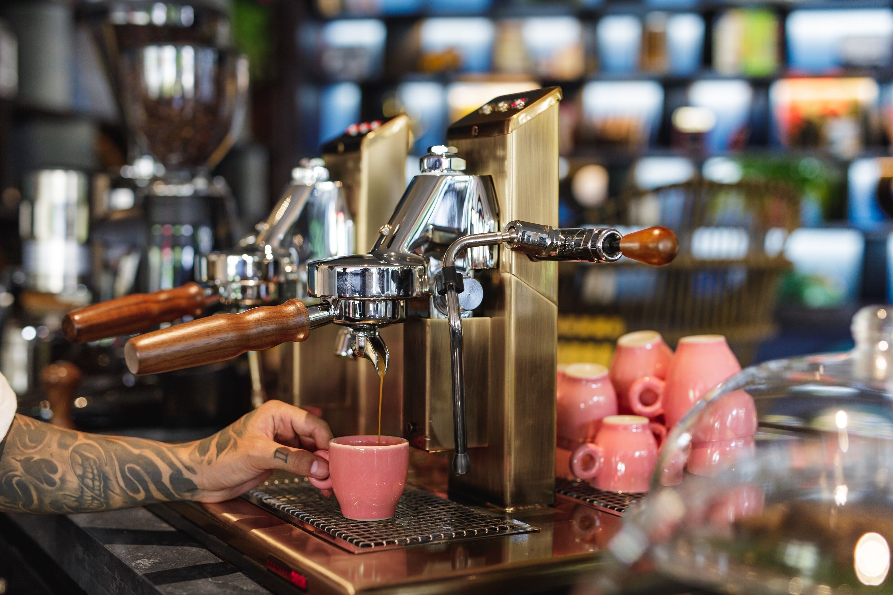 Eine Kaffeemaschine mit einer Hand, die eine rosa Tasse hält, und im Hintergrund mehrere Espressomaschinen.