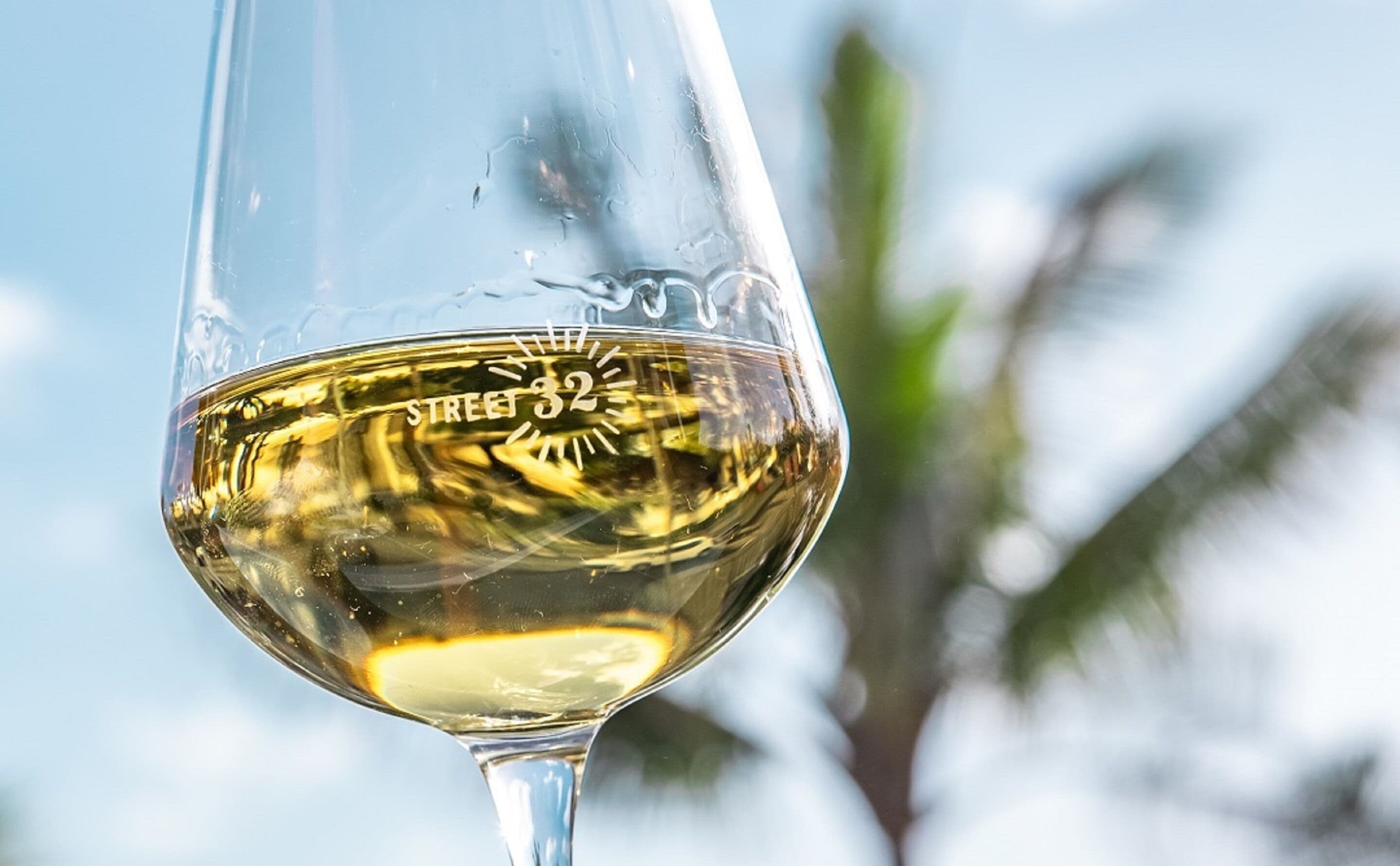 A clear glass of white wine with a reflection of palm trees and a clear sky in the background.