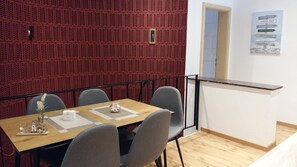 Een vergaderruimte met een houten tafel, grijze stoelen en een wand bekleed met rode akoestische panelen.