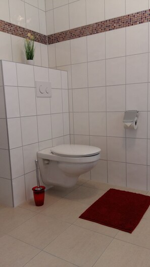 Een badkamer met een wit toilet, een rode mat en een betegelde muur met decoratieve rand.