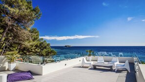 Una terraza en la azotea con vistas despejadas al mar, sillas de descanso blancas y una barandilla de vidrio.