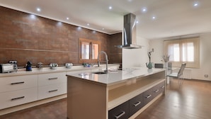A modern kitchen with a large island, built-in appliances, and a dining area with a chair and table. - CASA FENIX (Sant Josep de Sa Talaia / San Jose)