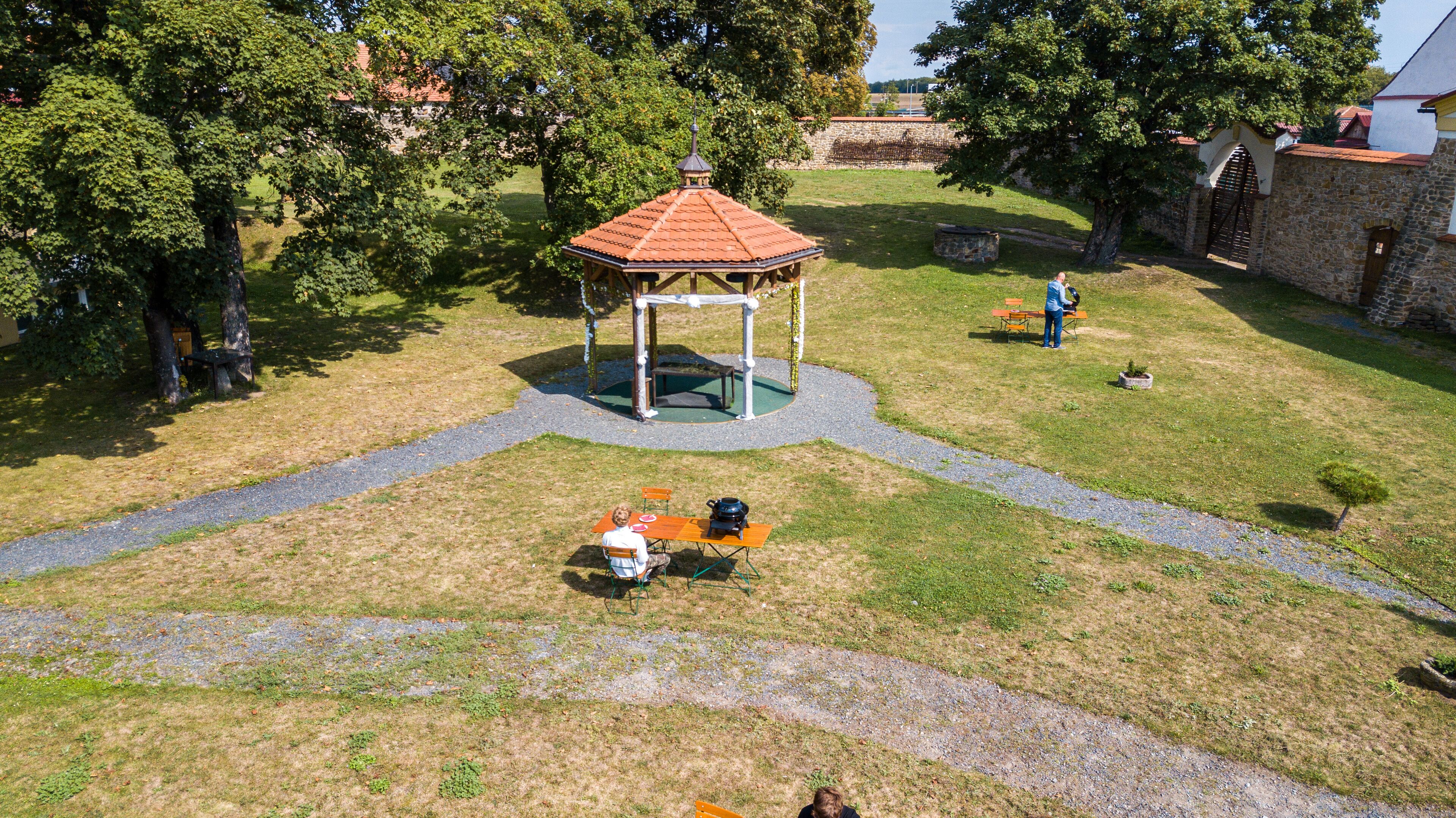 A gazebo with a tiled roof, surrounded by a grassy area with a paved path leading to it.