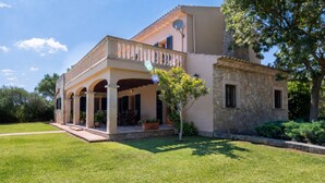 A two-story house with a covered patio, stone walls, and a well-maintained lawn. - Vela 1 Finca for 8 with pool in Playas de Muro (Muro)