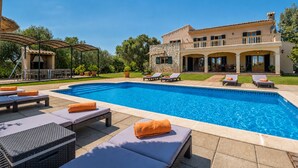 A swimming pool with lounge chairs and umbrellas, a stone building with balconies, and a well-maintained lawn. - Vela 1 Finca for 8 with pool in Playas de Muro (Muro)