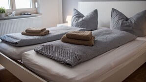 A neatly made double bed with striped bedding and folded towels, a white headboard, and a window with a view of the outside. - Schlafplätzle (Karlstadt)