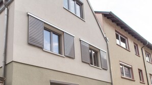 A multi-story building with a beige facade, multiple windows with shutters, and a wooden bench outside. - Schlafplätzle (Karlstadt)