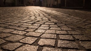 A cobblestone street leading to a building with a sun setting in the background. - Schlafplätzle (Karlstadt)