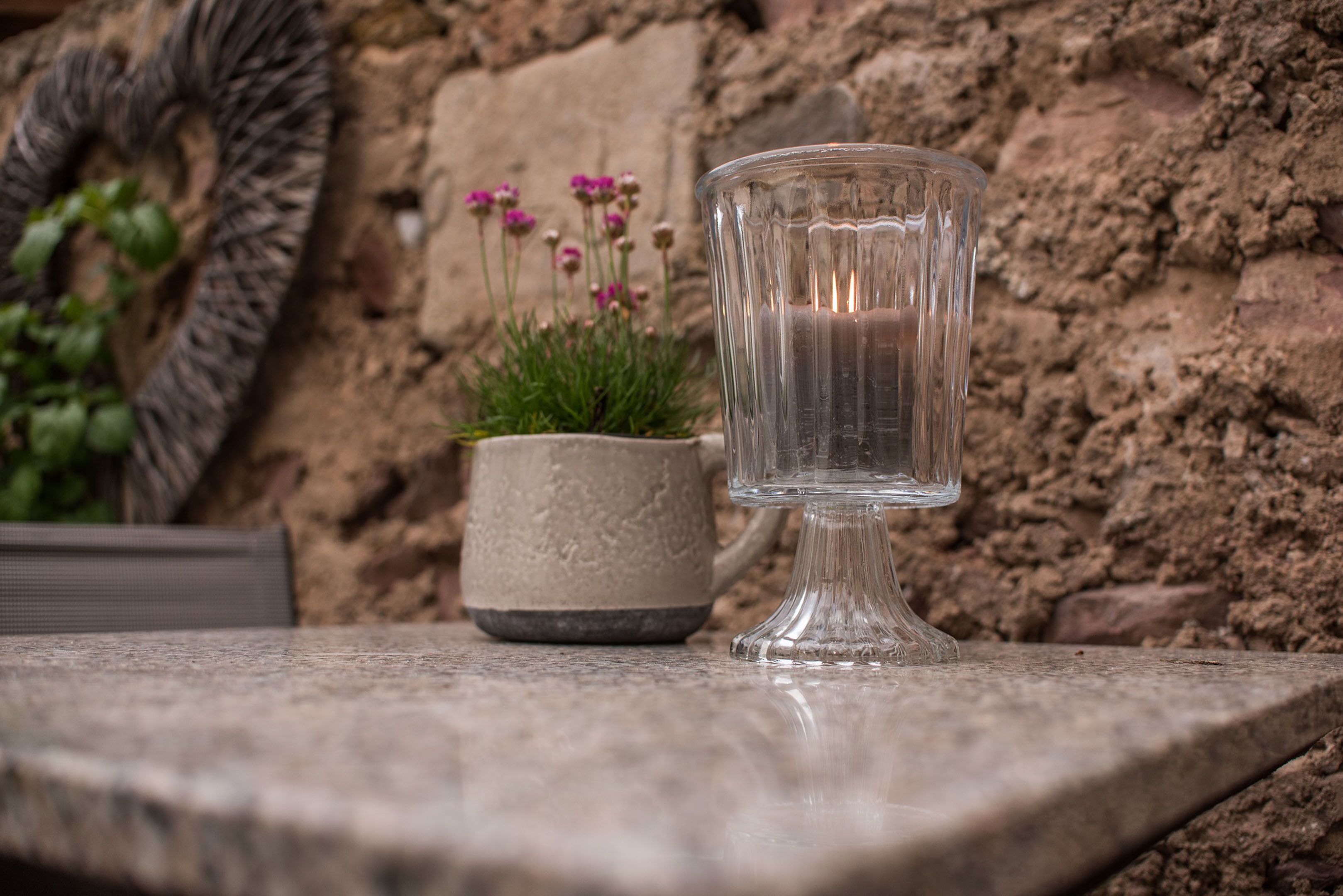 A clear glass mug on a stone surface with a textured stone wall in the background.