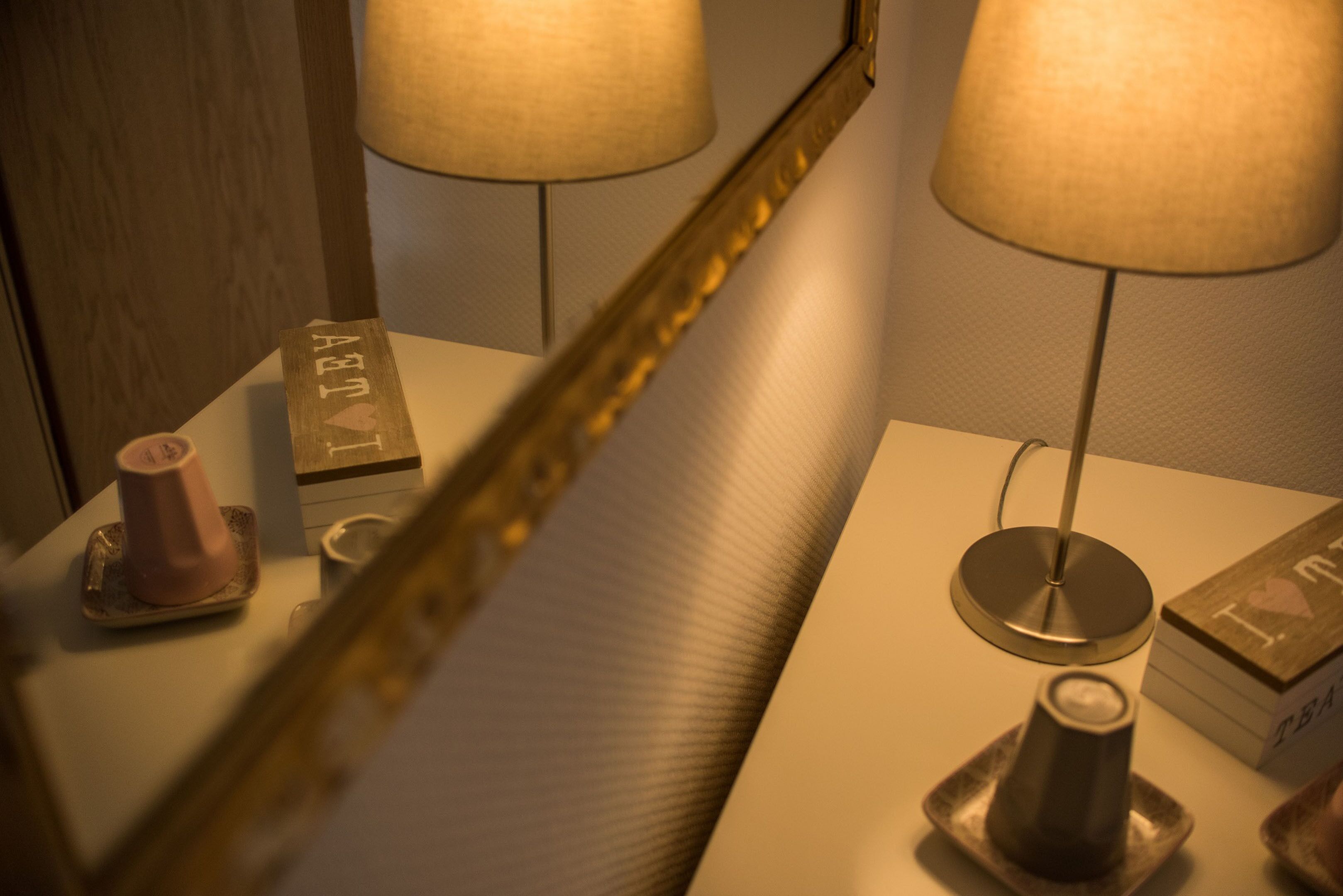 A room with a mirror reflecting a lamp and a small table with a candle holder.