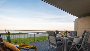A terrace with a table set for dining, chairs, and a lounge chair, overlooking a body of water. - Himmel & Meer - Terrace, Grill, Fireplace, Washing Machine, Underfloor Heating (Olpenitz)