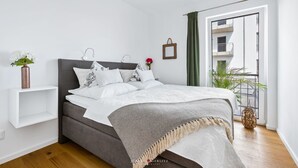 A modern bedroom with a grey bed, white bedding, a small plant, and a view of a balcony. - Himmel & Meer - Terrace, Grill, Fireplace, Washing Machine, Underfloor Heating (Olpenitz)