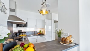 A modern kitchen with white cabinets, a stainless steel range hood, a microwave, and a fruit bowl on the counter. - Himmel & Meer - Terrace, Grill, Fireplace, Washing Machine, Underfloor Heating (Olpenitz)