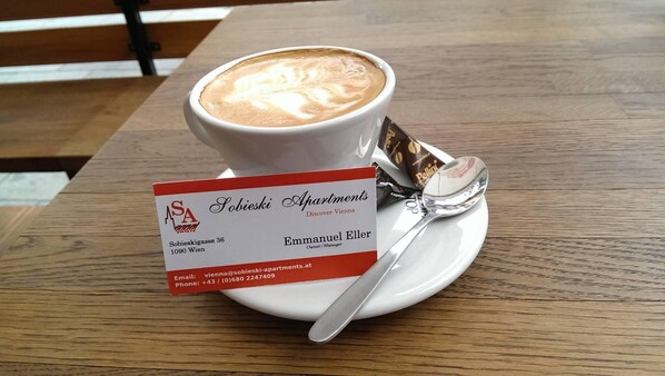 A business card for Sobieski Apartments with contact details, placed on a saucer next to a cup of coffee on a wooden table.