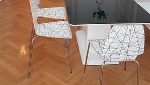 A dining area with a black table, white chairs with a geometric pattern, and a vase with flowers. - Extremely central 2 BR Apartment next to St  Stephen Cathedral (Vienna)
