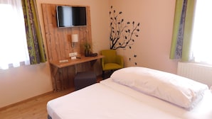A hotel room with a bed, a desk with a chair, a TV mounted on the wall, and a decorative tree decal.