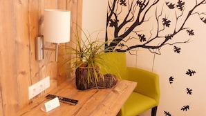 A wooden desk with a lamp, a potted plant, and a remote control. A green chair and a gray ottoman are also visible.