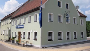 A two-story building with a green facade and a red-tiled roof. There is a sign for 'Gasthof Gruner Baum' on the left side, and a 'Tucker' sign on the right.