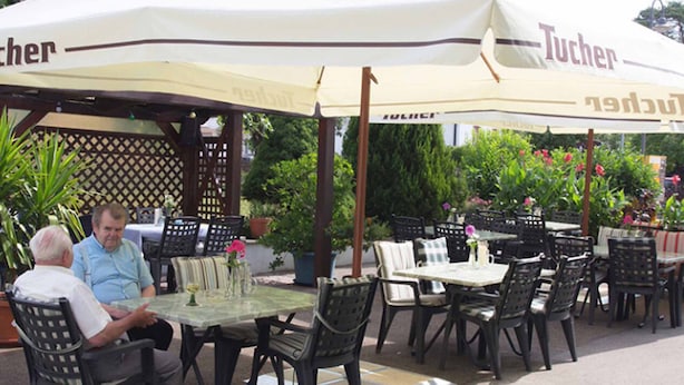 An outdoor seating area with tables and chairs under a large umbrella with 'Tucher' branding.