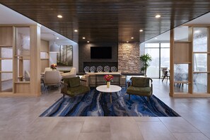 A modern interior with a stone accent wall, a flat-screen TV, and a blue patterned rug. - Fairfield Inn & Suites by Marriott Waller (Waller)