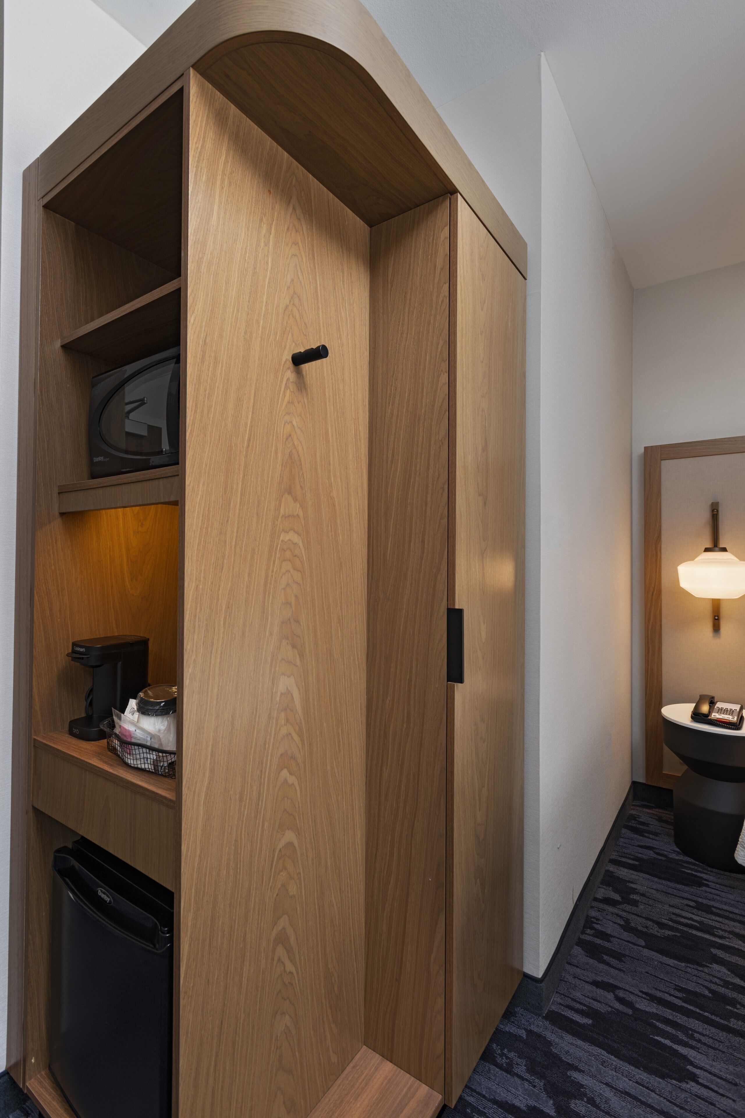 Ein Holzschrank mit schwarzem Griff, ein Ablagefach mit Kaffeemaschine und ein kleiner Mülleimer.
