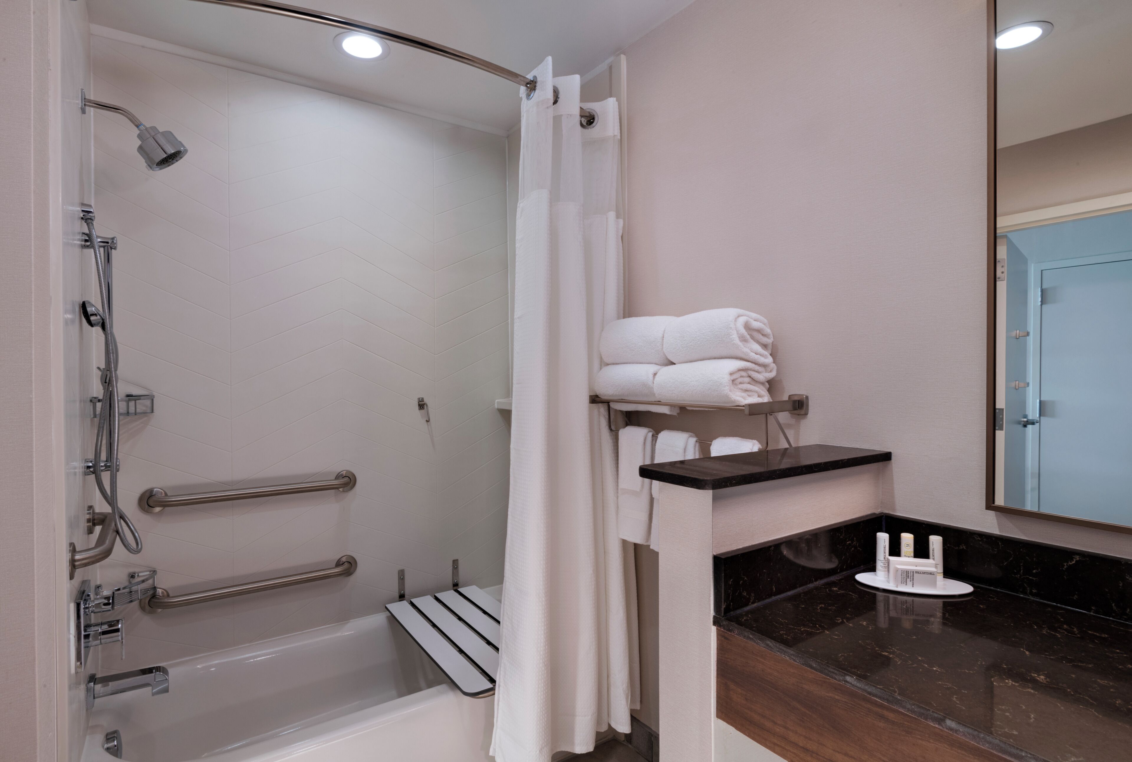 A modern bathroom with a shower, grab bars, a towel rack, and a vanity with a mirror.