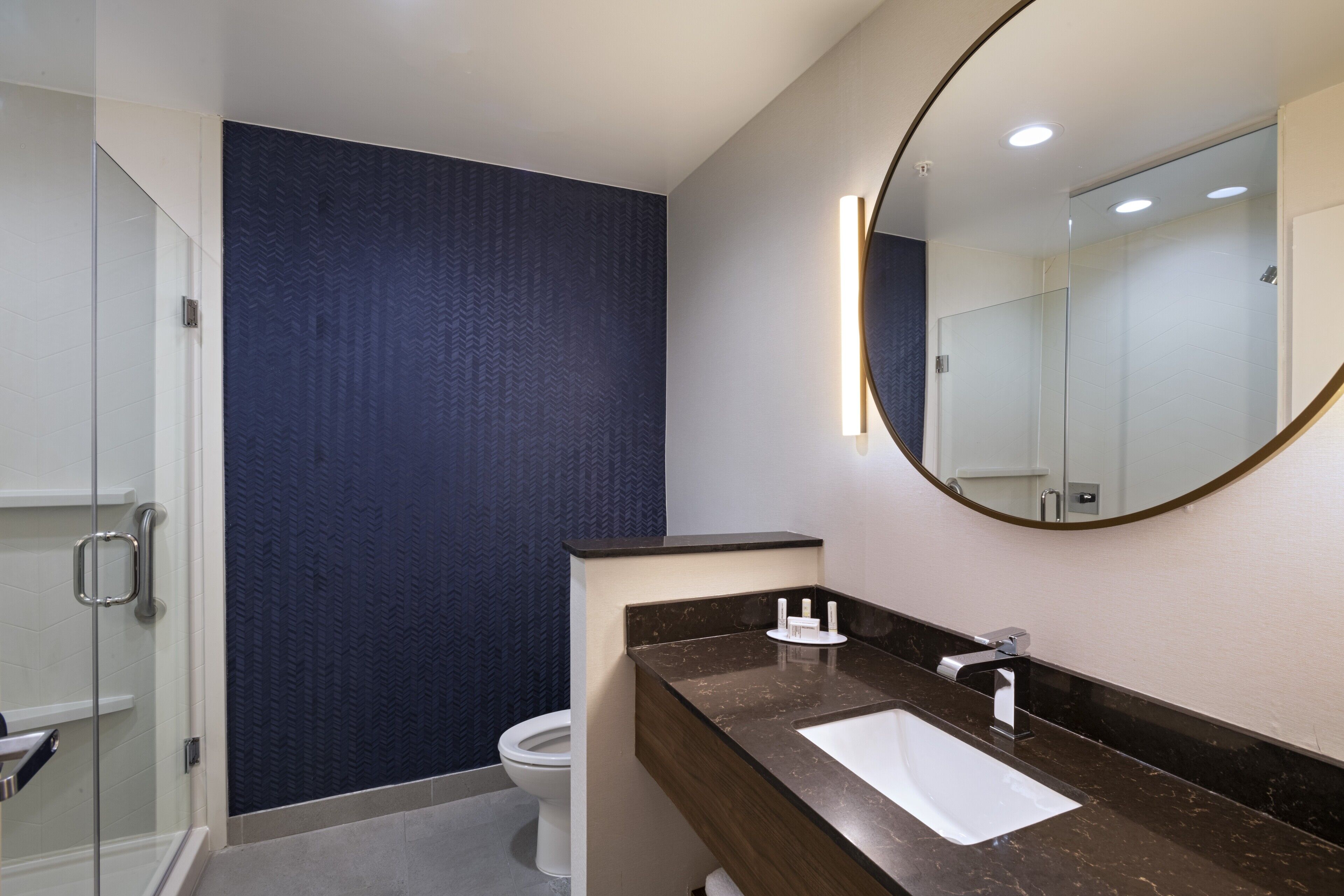 Un baño moderno con cabina de ducha de vidrio, un lavamanos blanco y un espejo grande con marco dorado.