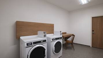 A laundry room with two front-loading washing machines, a wooden bench, and a desk.