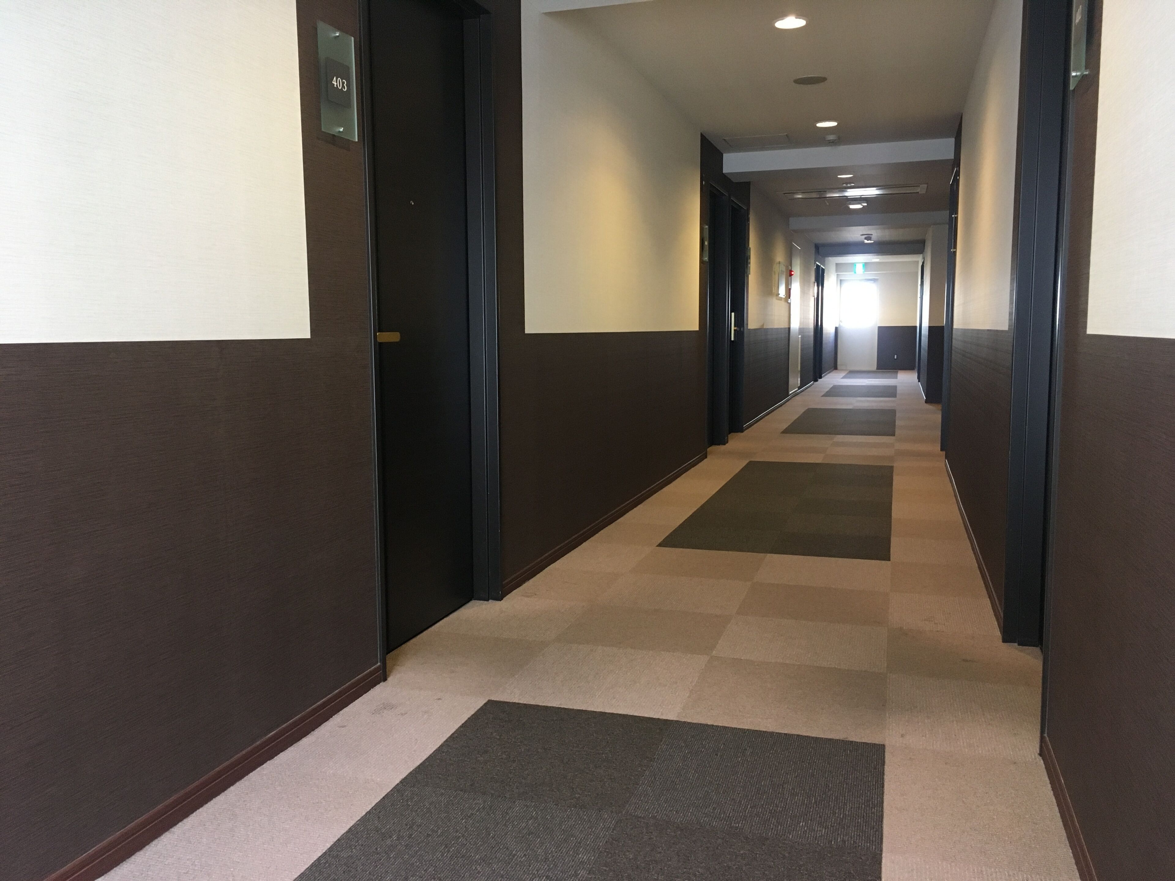 Un couloir d'hôtel avec des revêtements de sol en moquette, des murs sombres et des portes de part et d'autre.