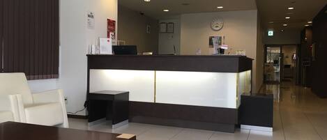 Un área de recepción con mostrador, un reloj en la pared y un espacio de espera con mesa y sillas.