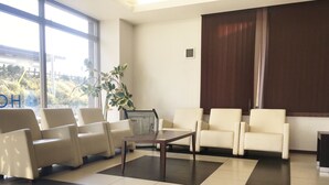 A waiting area with a check-in counter, several chairs, a coffee table, and a large window with blinds. - Hotel Aisis Kakegawa (Kakegawa)