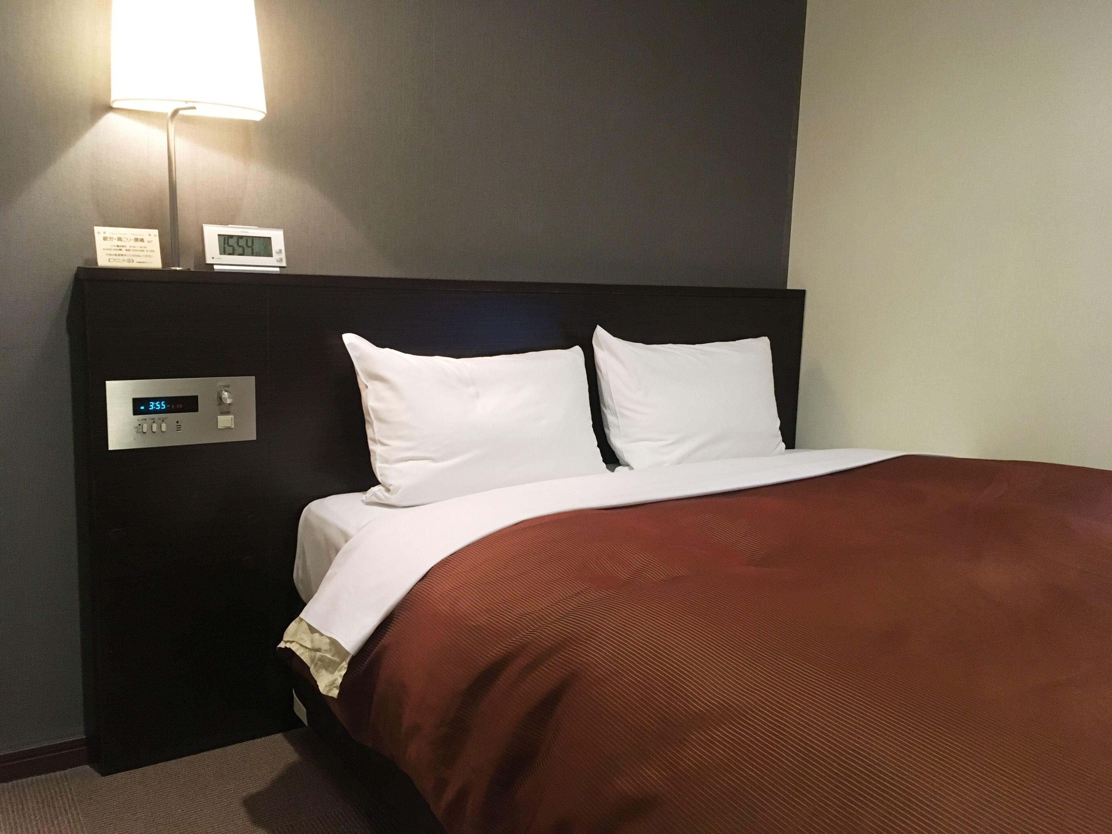 A hotel room with a bed, a digital clock, and a control panel.