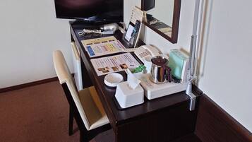A hotel room with a desk, a television, a telephone, a mirror, a coffee maker, and a bedside table.
