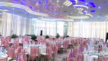 A banquet hall with round tables, pink chair covers, and a modern ceiling design.