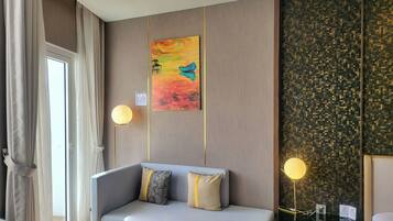 A modern hotel room with a grey sofa, two pillows, a painting, a wall with a pixelated pattern, and two wall-mounted lamps.