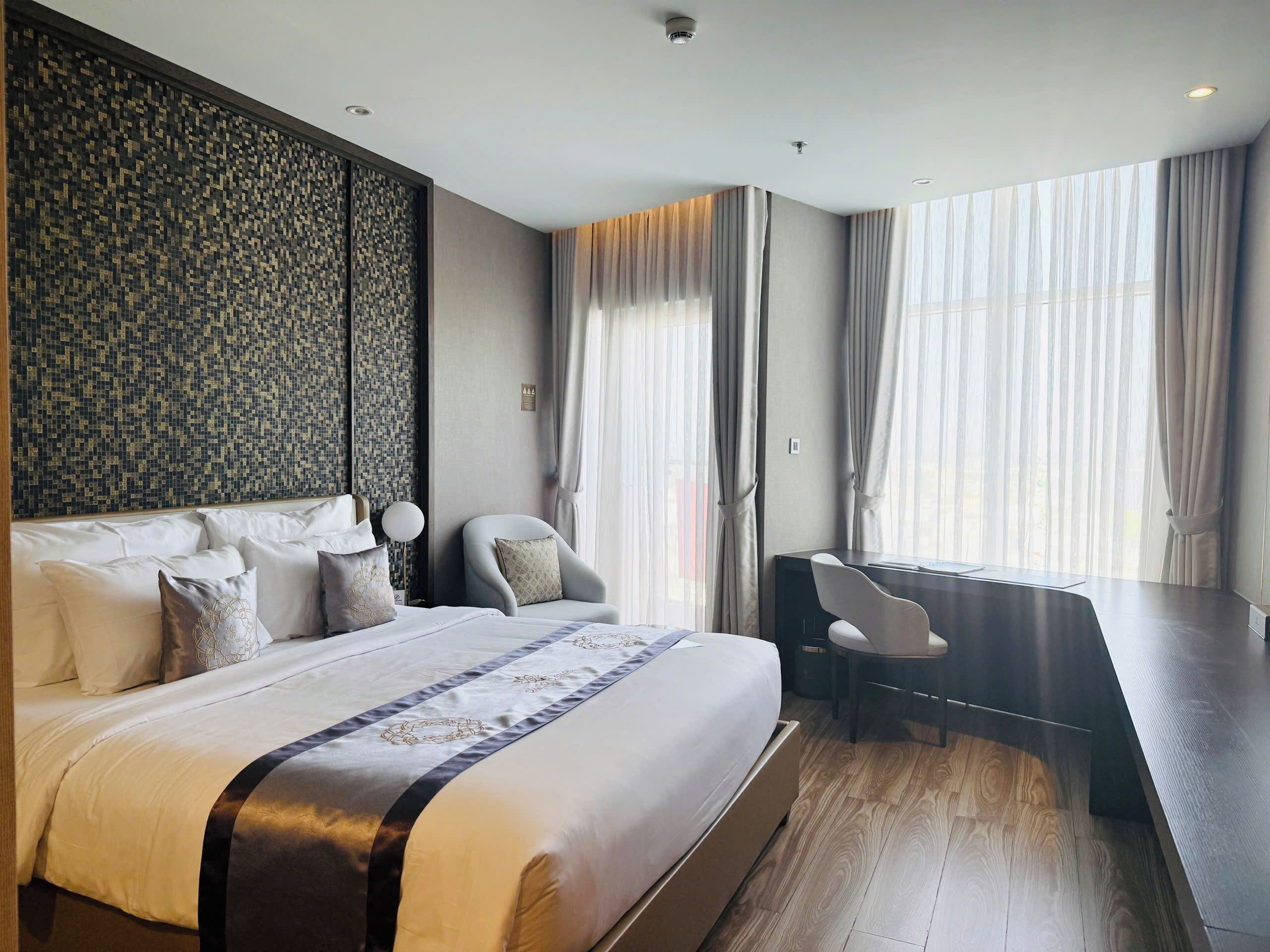 Een moderne hotelkamer met een groot bed, een bureau en een uitzicht op de stad door grote ramen.