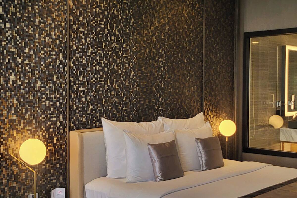A modern hotel room with a large bed, a dark textured wall, and a large mirror.