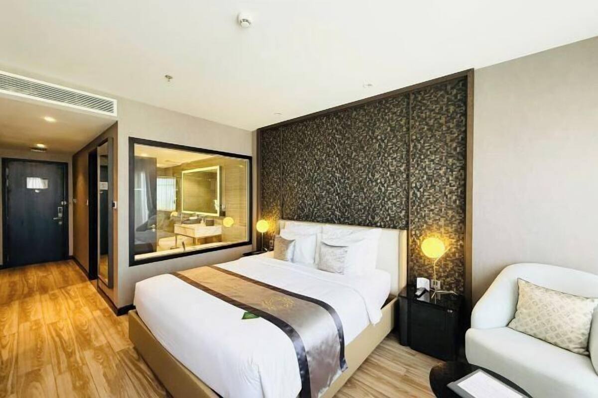 A hotel room with a large bed, a bedside table with a lamp, a mirror, and a seating area with a chair.