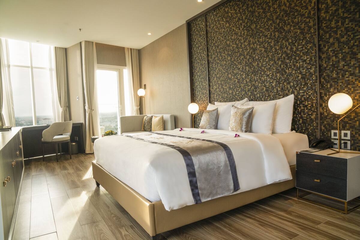 A modern hotel room with a large bed, a desk, and a view of the city.