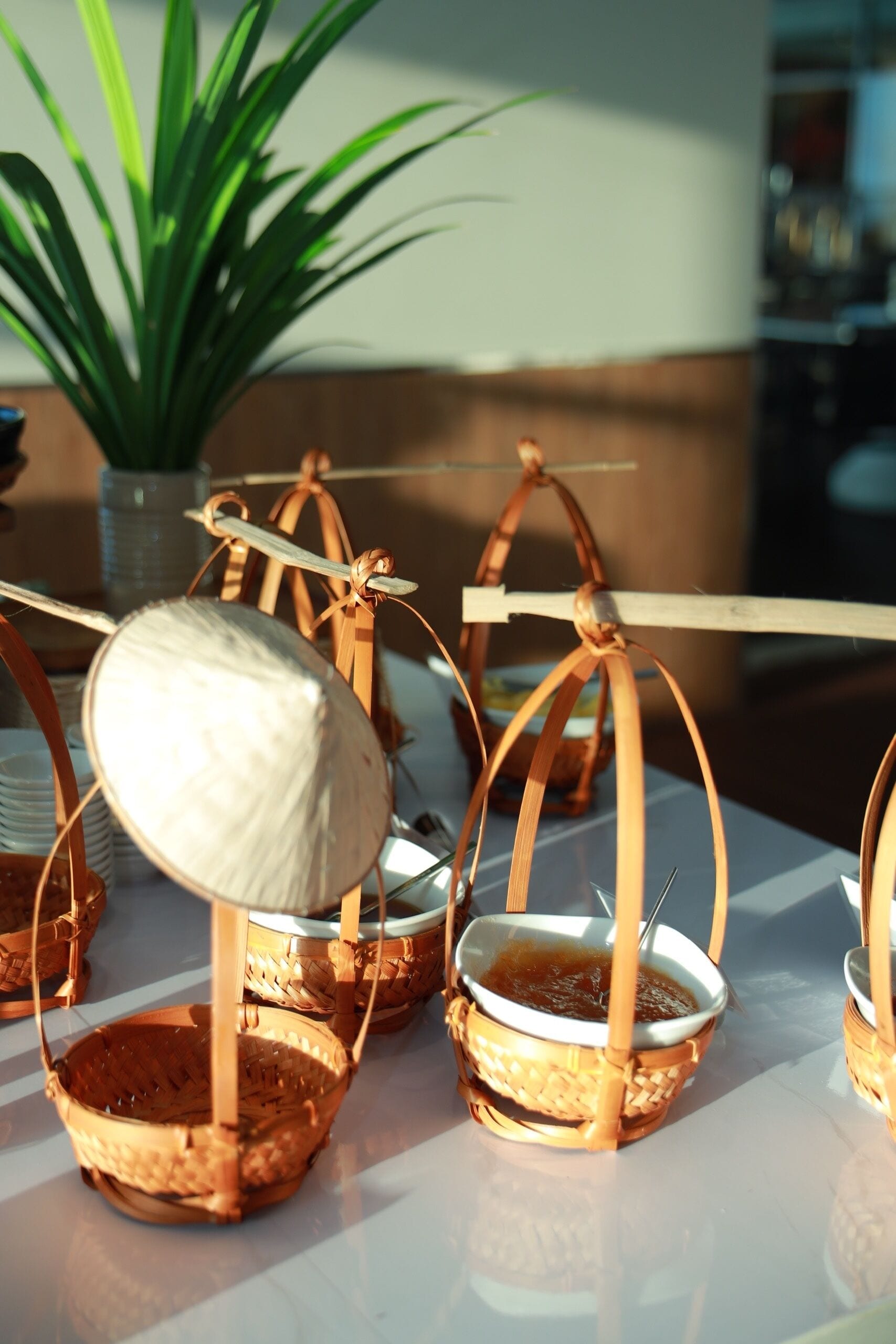 A table with several small woven baskets, some containing a white object, and a potted plant in the background.