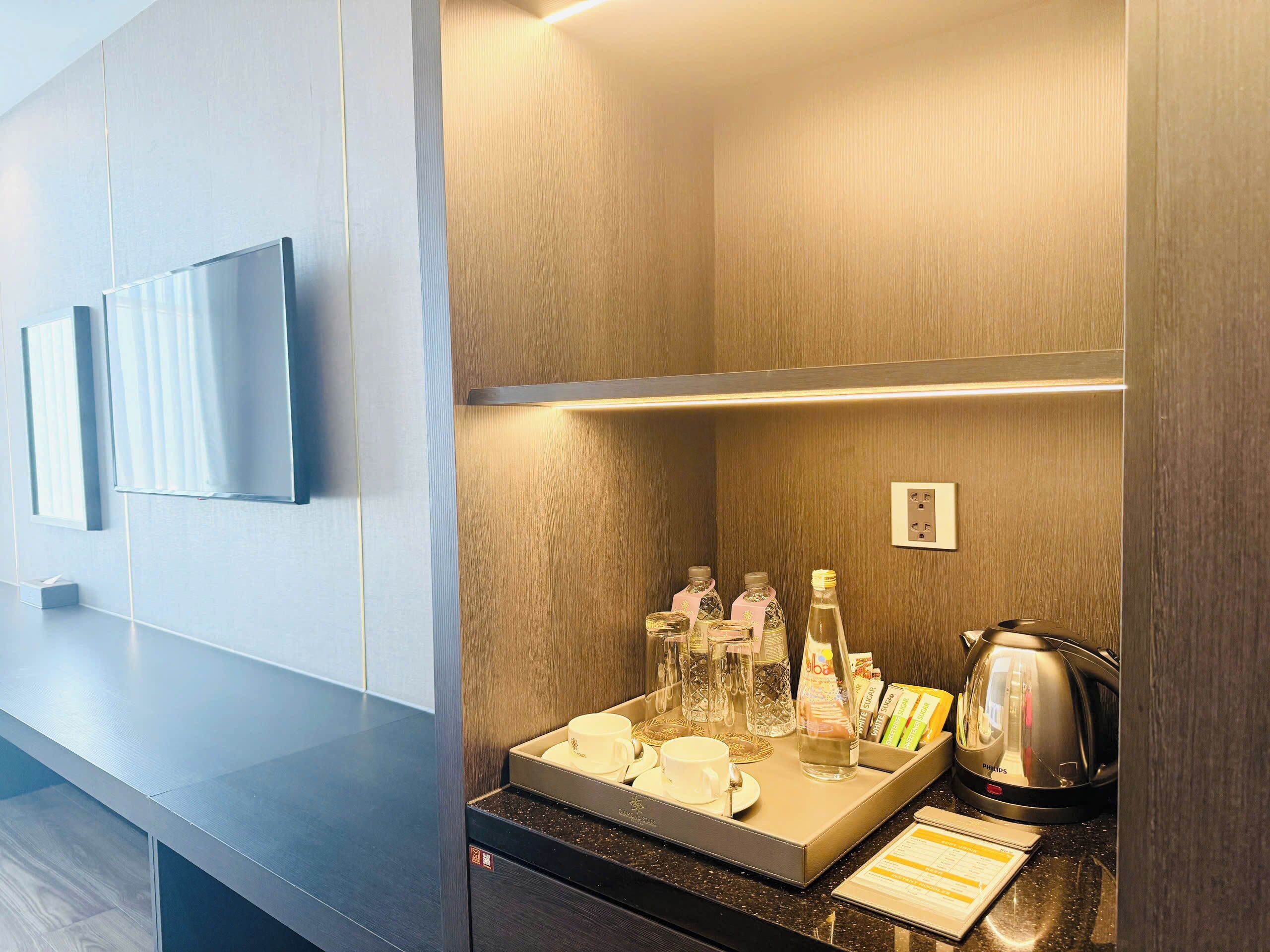Une chambre d’hôtel dotée d’un téléviseur à écran plat fixé au mur, d’un coin café avec une bouilloire et des tasses, et d’un mur recouvert de panneaux en bois.